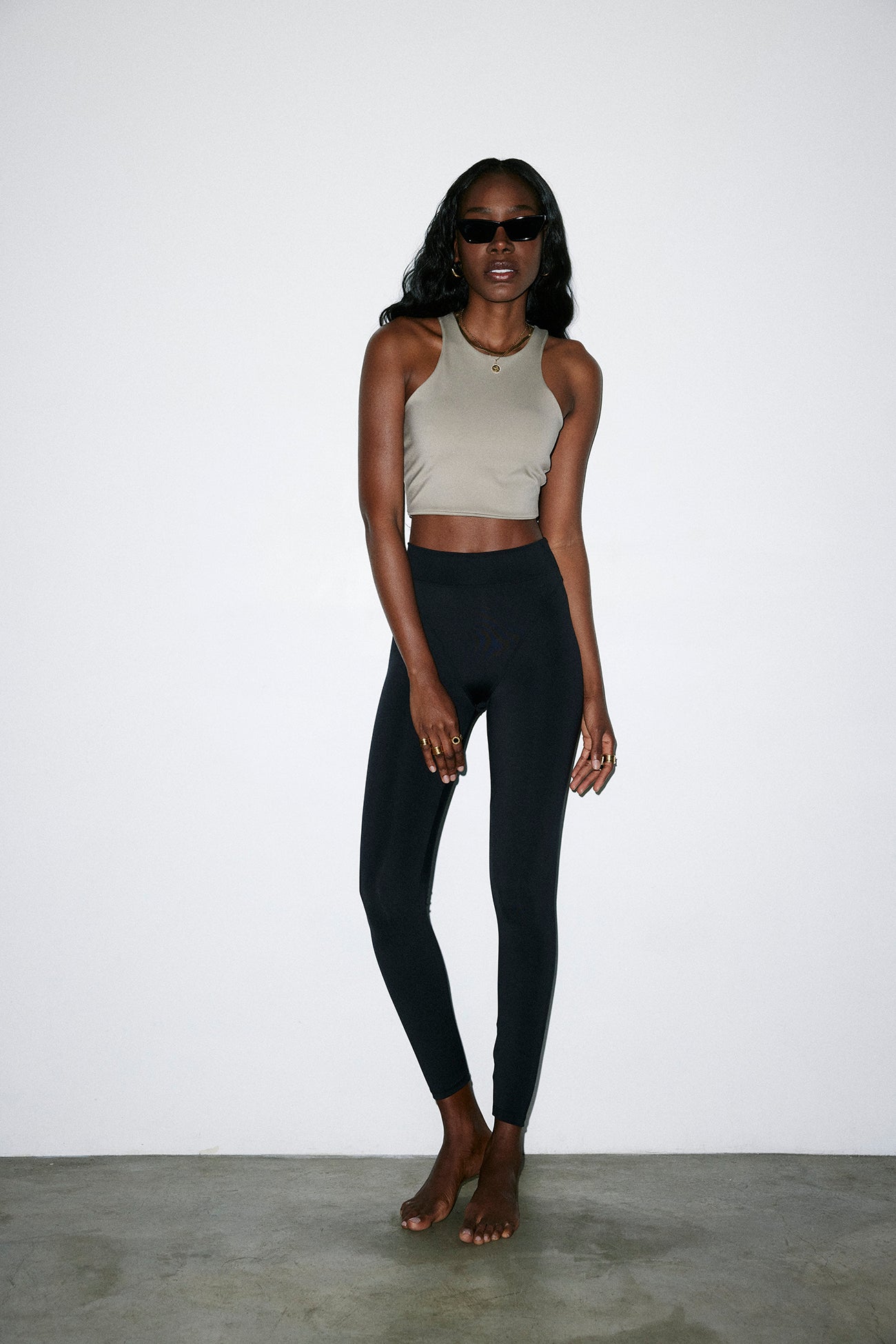 Person wearing a beige tank top and black leggings against a white background