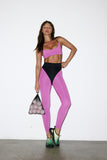 Woman wearing pink sports bra and leggings holding a bag against a white background
