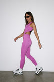 Woman wearing a pink athletic outfit with black sunglasses against a white background