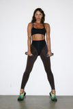 Woman in black athletic top and leggings holding dumbbells against a white background
