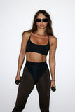 Person wearing a black sports bra and leggings with sunglasses on a white background