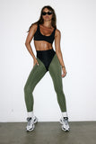 Woman wearing a black sports bra and green leggings against a white background