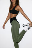 Person wearing black sports bra and green leggings with white sneakers on a white background