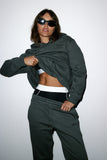 Person wearing a dark green jacket and pants with sunglasses on a white background