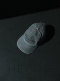 A washed black baseball cap with the HÉROS logo embroidered on the centre front, displayed on a dark background with the word 'HÉROS' also printed beside the cap.