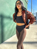A model wearing high-waist brown leggings and a brown crop jacket, standing against a green backdrop.