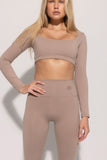 A female model wearing a beige long-sleeve sports top and matching leggings with a high-waisted fit. The outfit is part of a pre-sale collection.