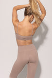 A sports bra in a neutral color, presumably beige or clay, showcasing the back view with adjustable straps and a central brand logo.