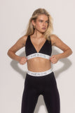 A female model wearing a black sports bra with 'HEROES' branding on the elastic band, posing against a white background.