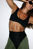Woman wearing a black sports bra and green leggings against a white background