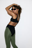 Woman wearing a black sports bra and green leggings on a white background